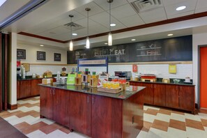 Ein Frühstücksbuffet mit einer Kreidetafel-Speisekarte, verschiedenen Speisen und einem Schild mit der Aufschrift 'Happy Breakfast Starts Here'.