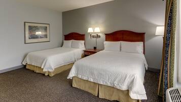 A hotel room with two beds, a nightstand, a lamp, and a painting on the wall.