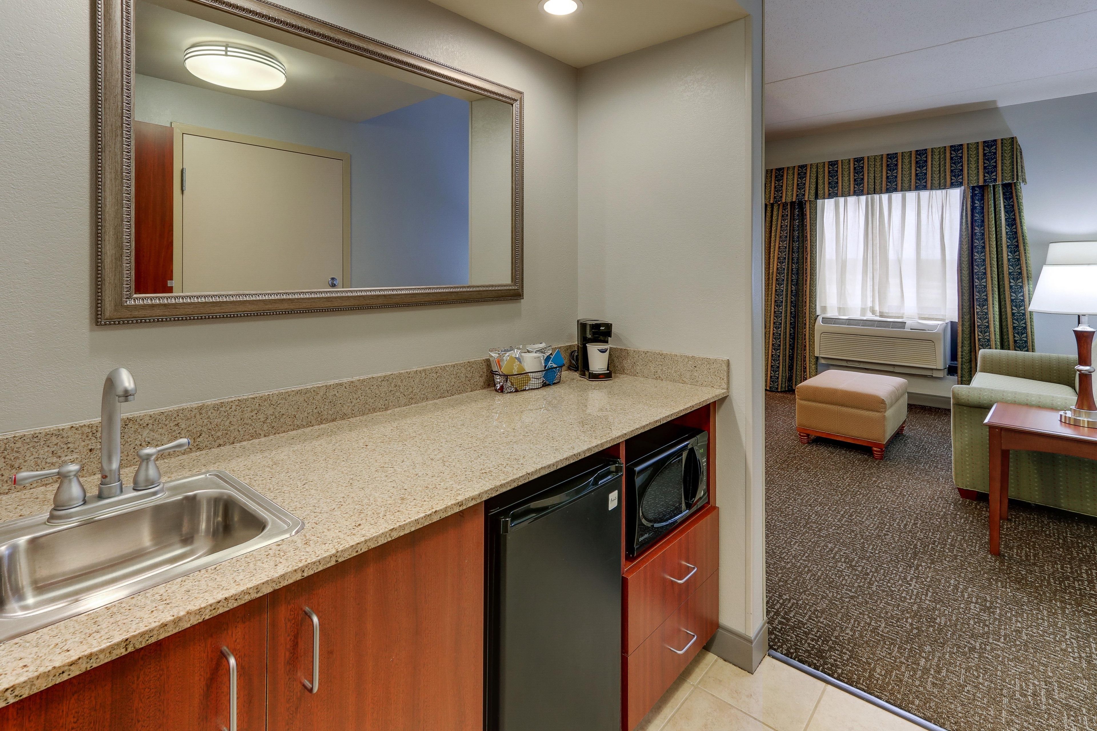 A compact kitchen with a sink, dishwasher, and microwave. A large mirror hangs above the counter.