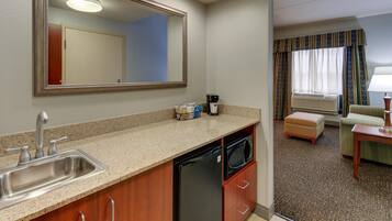 A compact kitchen with a sink, dishwasher, and microwave. A large mirror hangs above the counter.