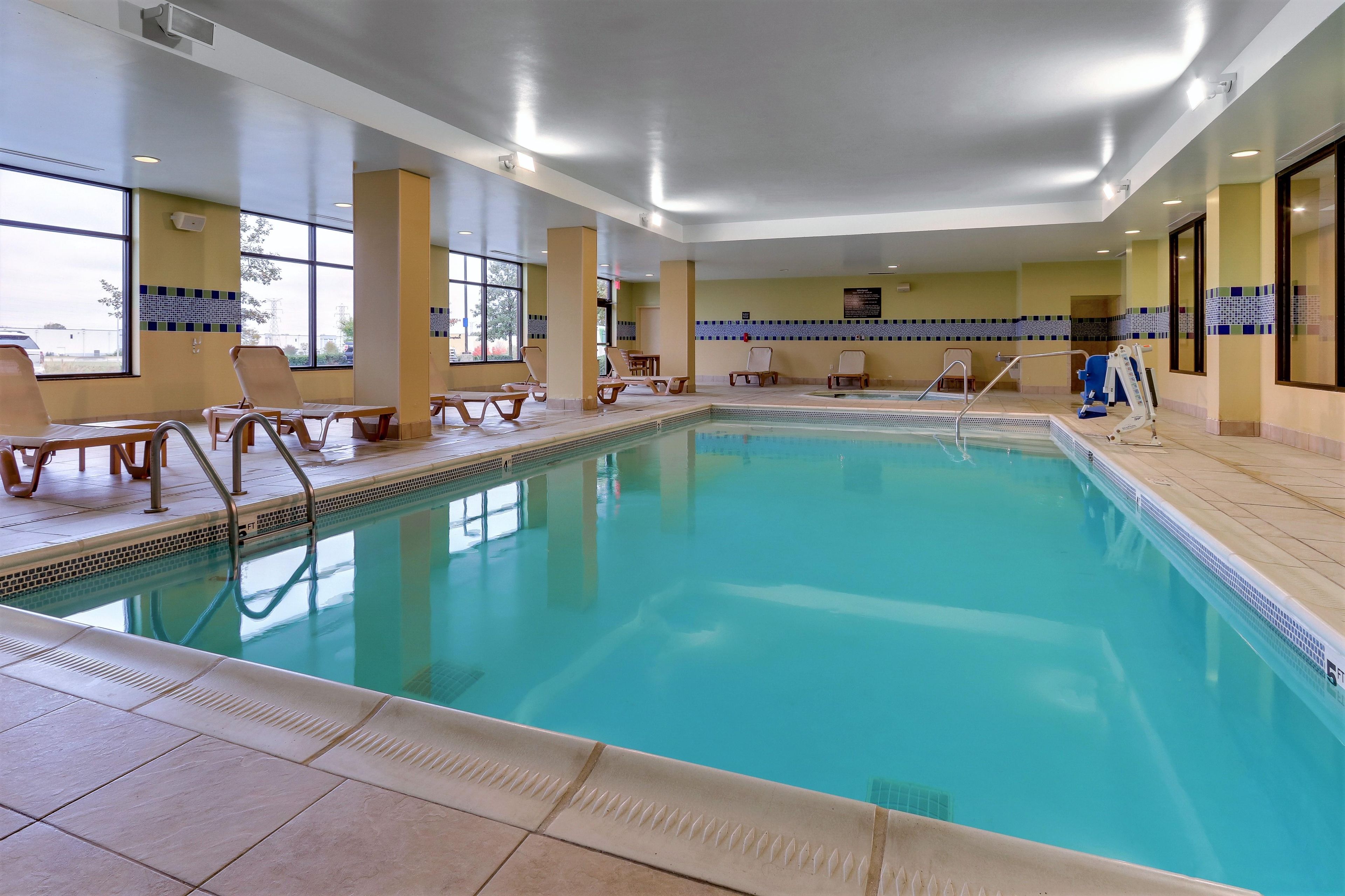 Una piscina interior con agua cristalina, rodeada de sillones de descanso y un suelo de baldosas.
