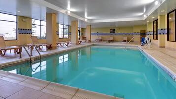 Una piscina interior con agua cristalina, rodeada de sillones de descanso y un suelo de baldosas.