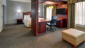A hotel room with a bed, desk, chair, ottoman, and a TV. - Hampton Inn & Suites Indianapolis-Airport (Indianapolis)