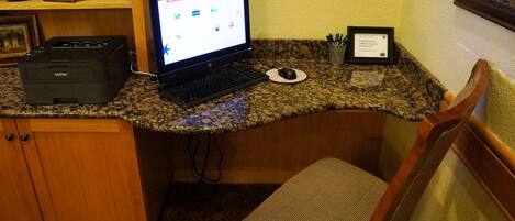 A workspace with a desktop computer, printer, and a framed certificate on a granite countertop.