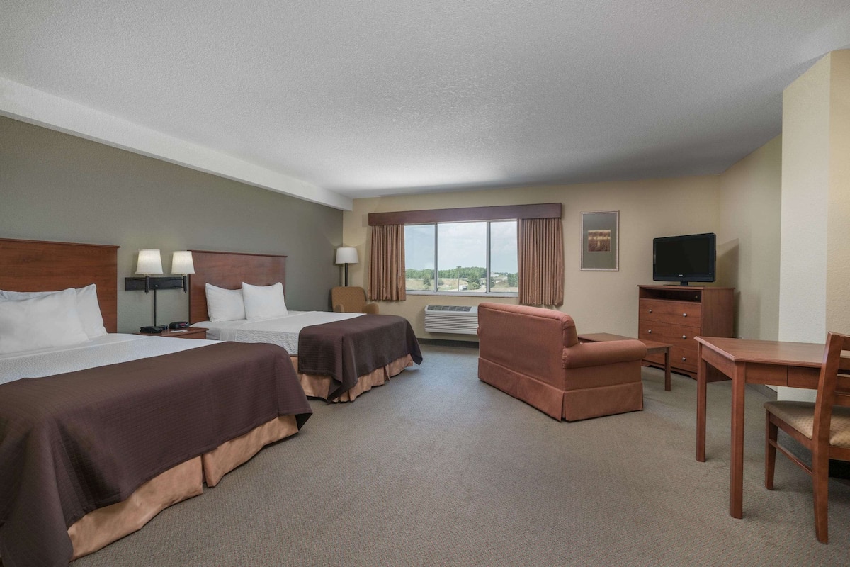 Habitación de hotel con dos camas, un sofá, un escritorio, un televisor y una ventana con cortinas.