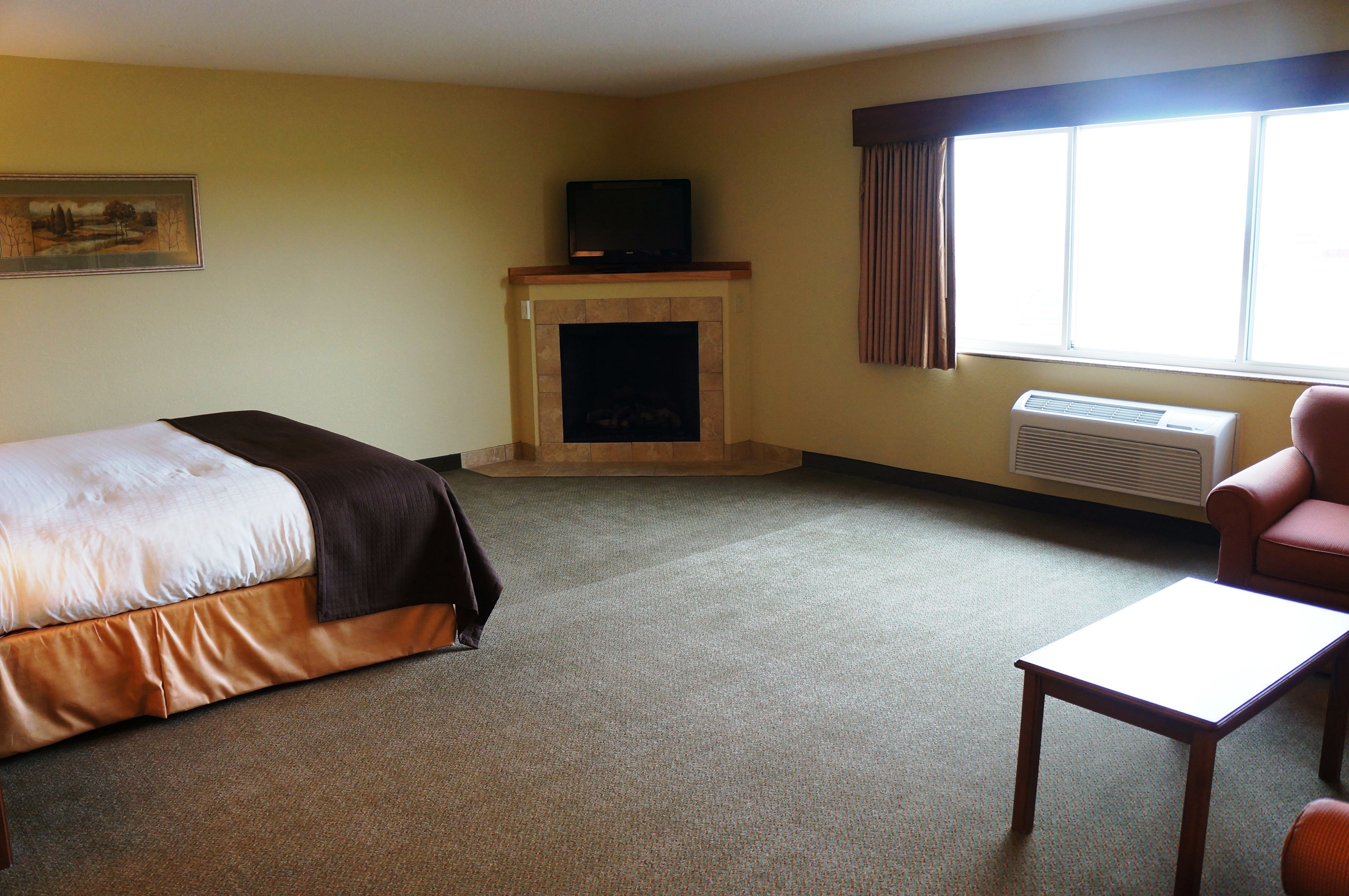 A hotel room with a bed, a fireplace, a television, a window with curtains, and a chair.