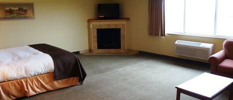 A hotel room with a bed, a fireplace, a television, a window with curtains, and a chair.