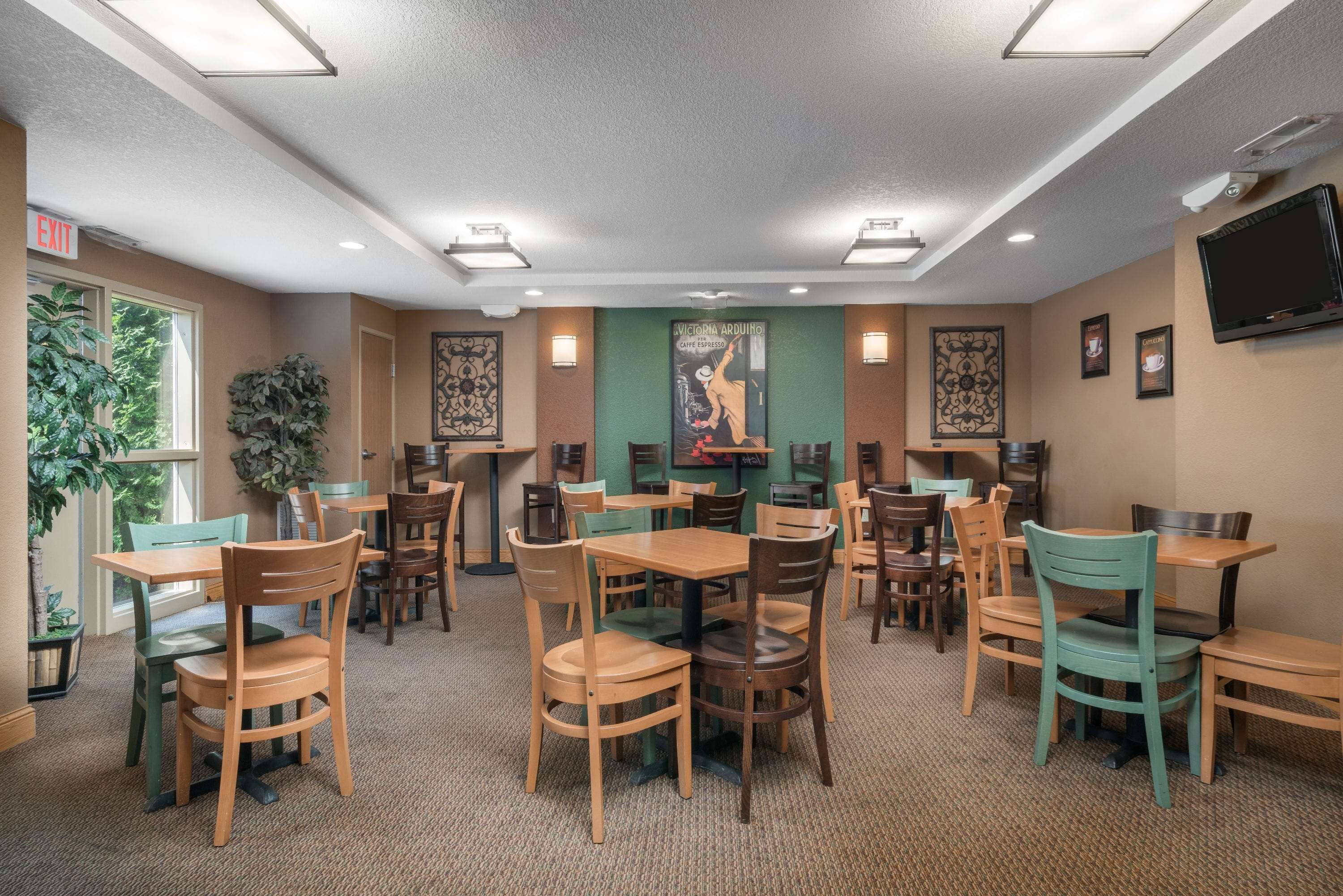 A restaurant with multiple tables and chairs, a television mounted on the wall, and a green wall with a poster.