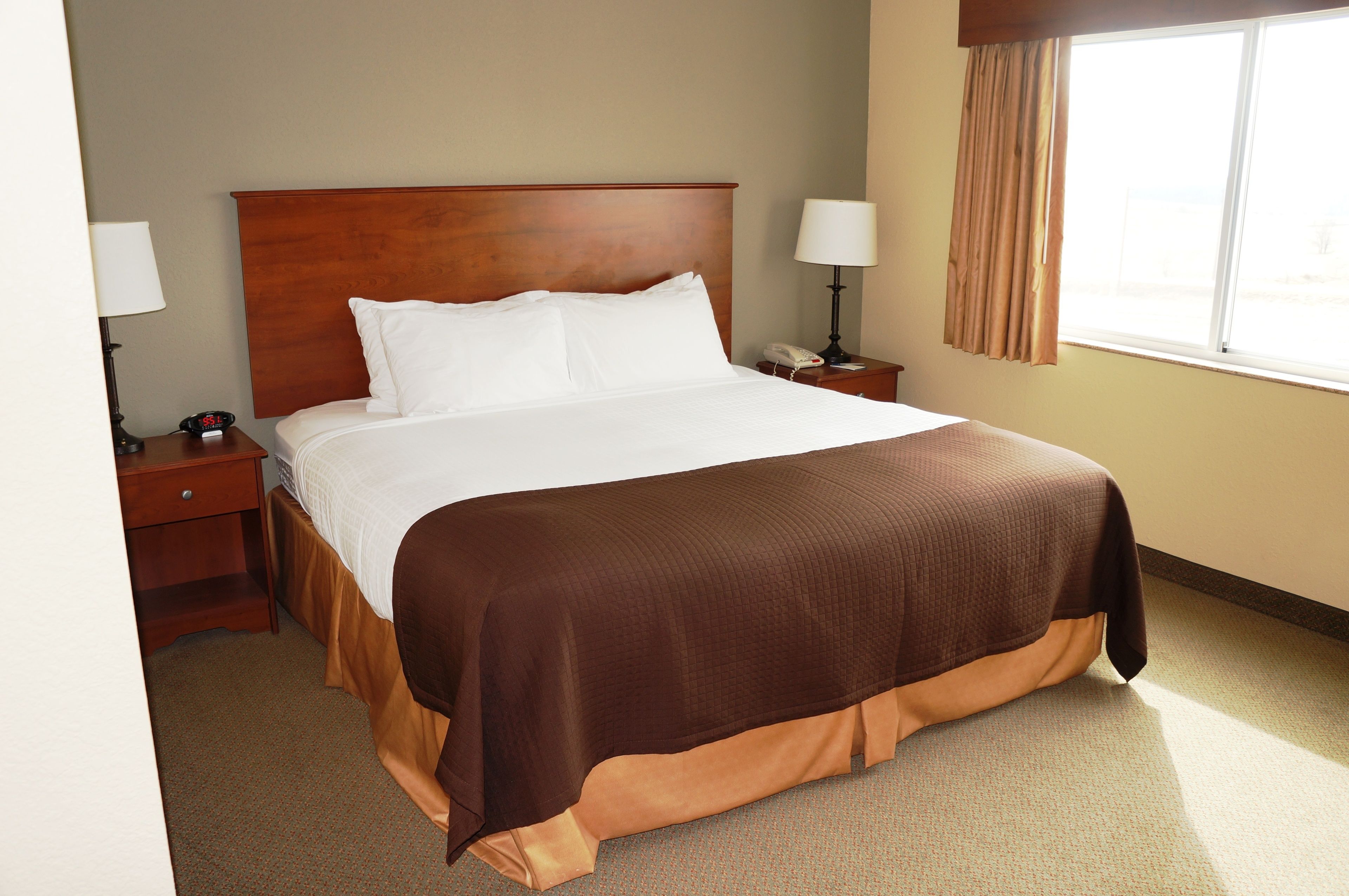 A hotel room with a large bed, a nightstand with a lamp, a telephone, and a window with curtains.