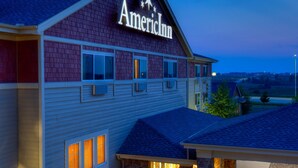 A two-story building with a sign reading "American Inn." It features a covered front porch with a stone facade and a clear view of the surrounding landscape. - AmericInn by Wyndham Newton (Newton)
