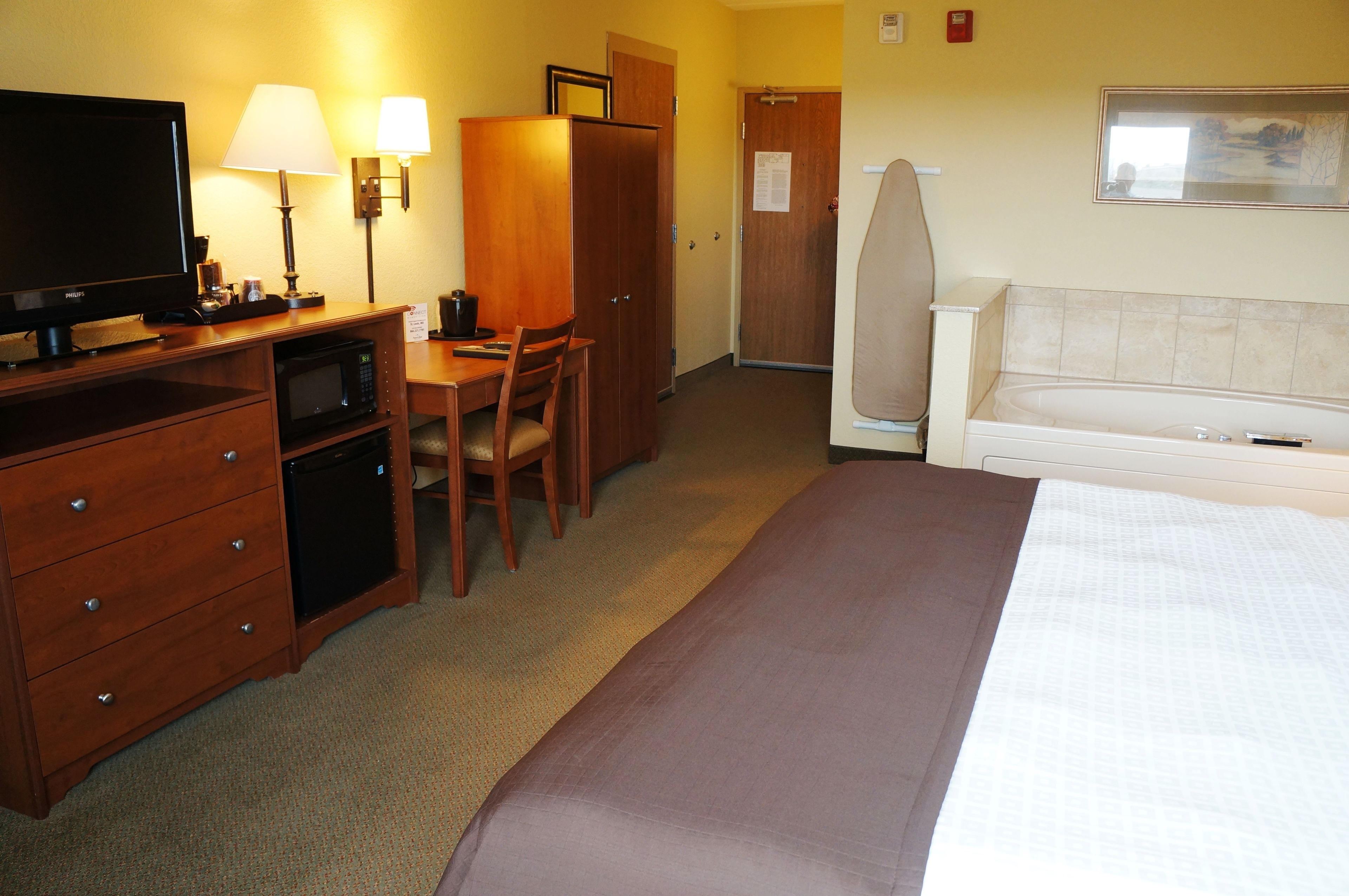 Une chambre d’hôtel comprenant un lit, un bureau avec une télévision, un micro-ondes, une armoire et un coin salon avec un fauteuil.