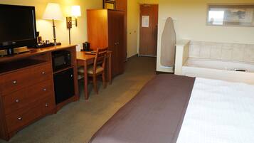 A hotel room with a bed, a desk with a television, a microwave, a wardrobe, and a seating area with a chair.