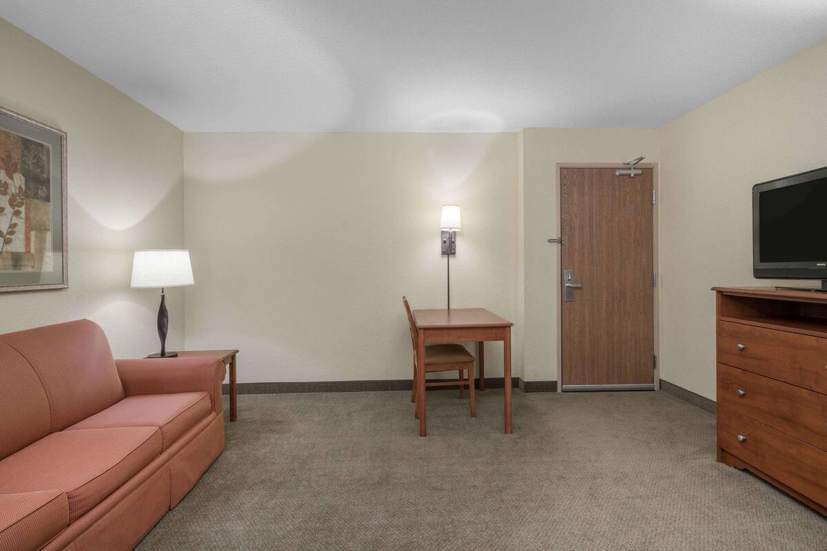Una habitación con sofá, escritorio, silla, televisor y puerta.