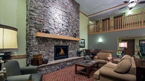 A cozy living room with a stone fireplace, comfortable seating, and a wooden ceiling fan. - AmericInn by Wyndham Newton (Newton)