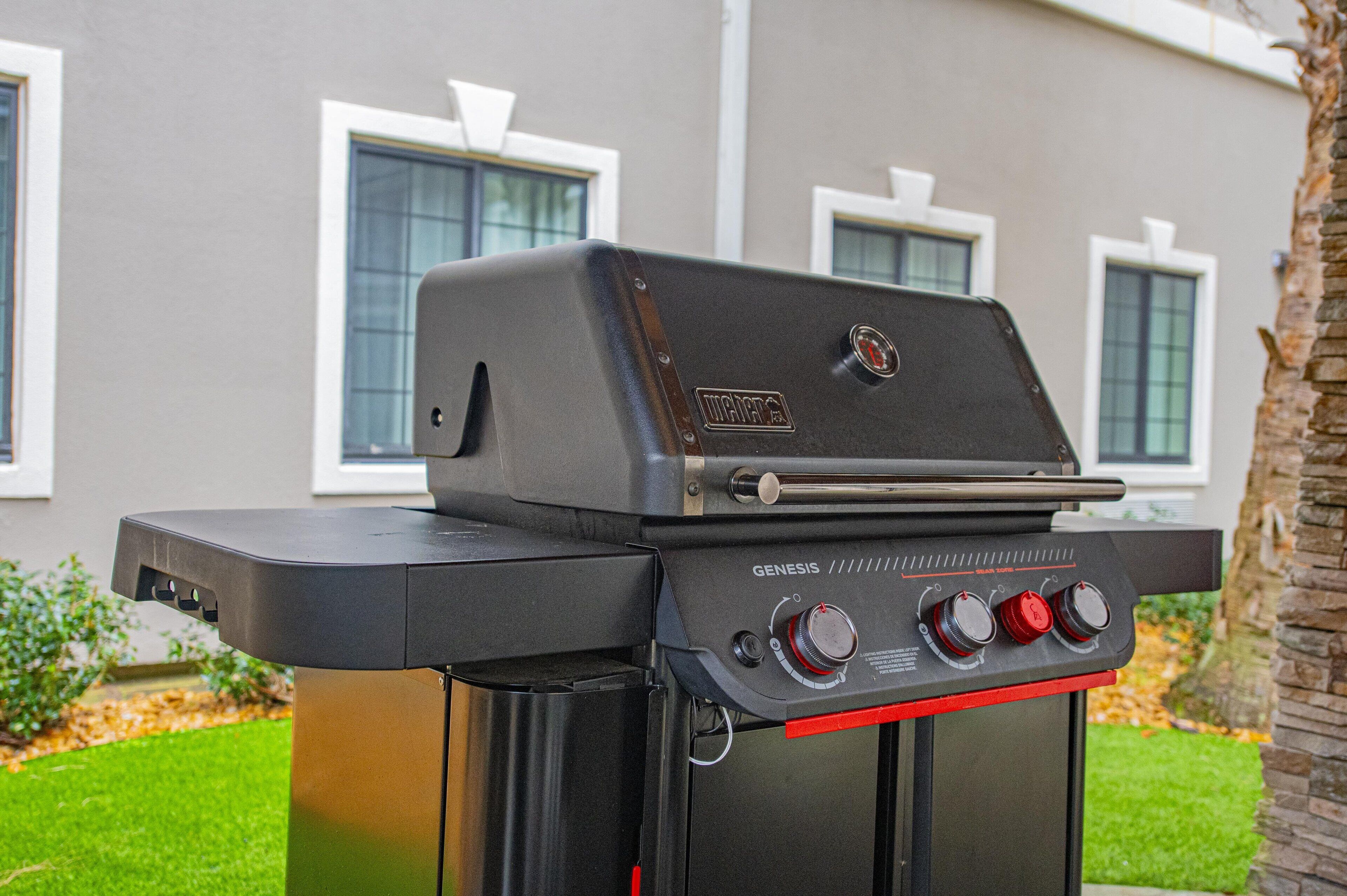 Un barbecue portable de la marque Genesis, doté d’un écran numérique et de boutons de contrôle, est présenté devant une maison aux fenêtres blanches et dont la pelouse est parfaitement entretenue.
