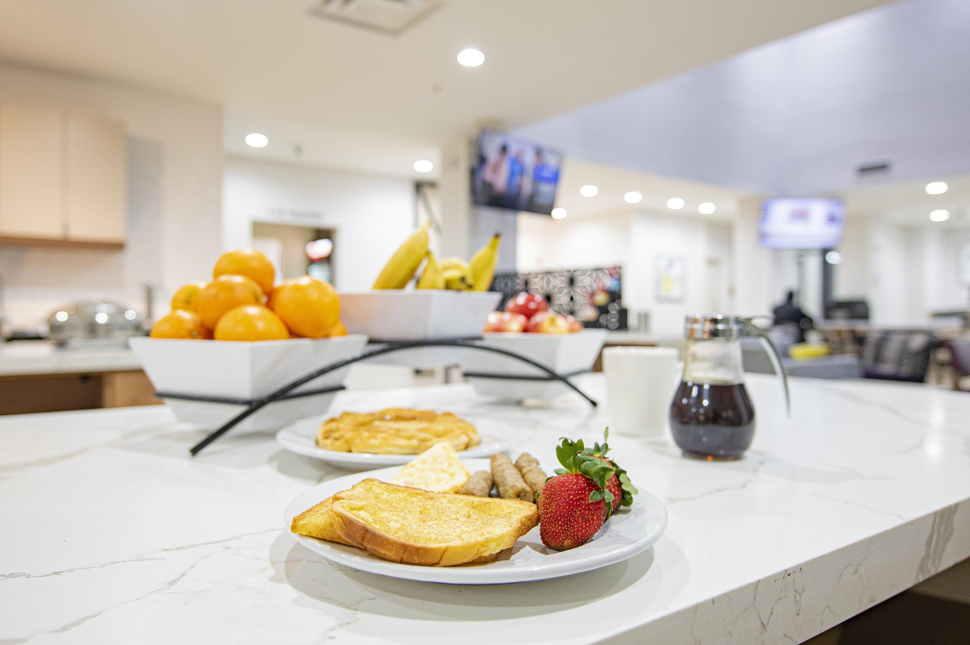 Un plateau de petit-déjeuner avec des toasts, des fraises et un bol rempli d’oranges et de bananes, le tout posé sur un comptoir en marbre.