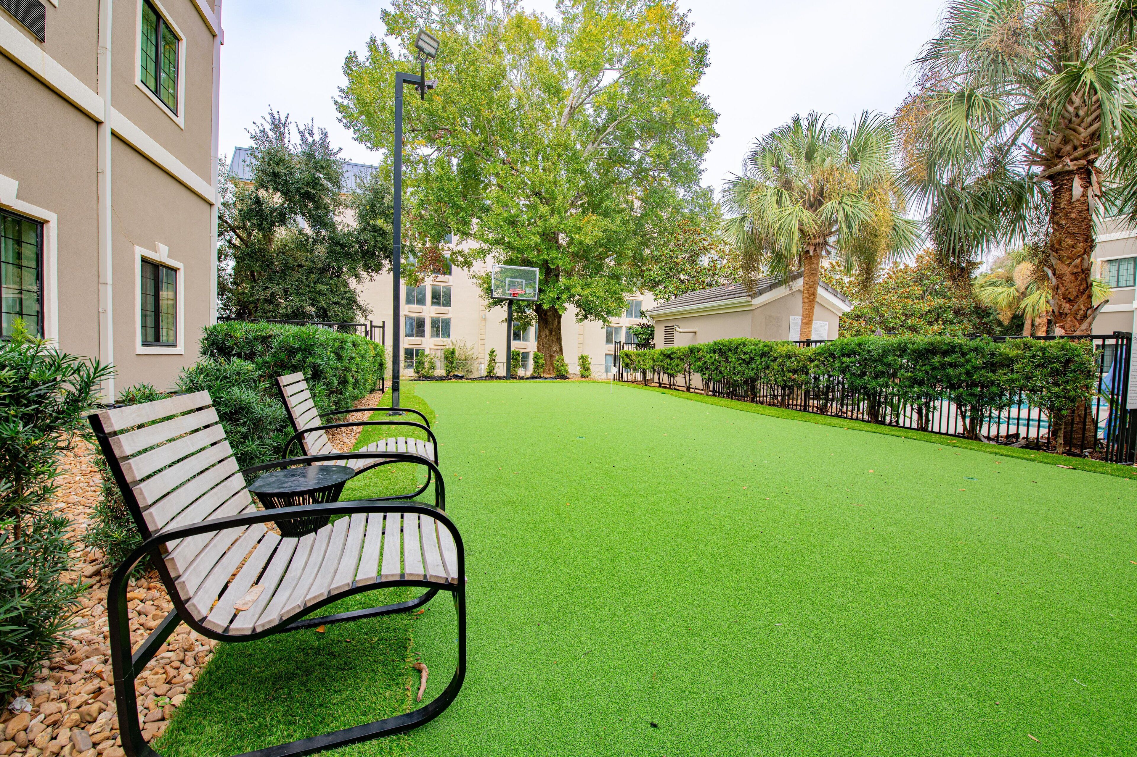 A courtyard with artificial green turf, a basketball hoop, and a seating area with benches.