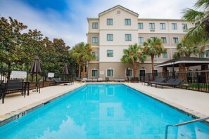 A swimming pool with lounge chairs and umbrellas, surrounded by palm trees and a multi-story building. - Staybridge Suites Lafayette by IHG (Lafayette)
