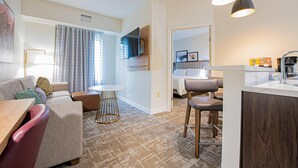 A modern hotel room with a living area, kitchenette, and a view of the city. - Staybridge Suites Lafayette by IHG (Lafayette)