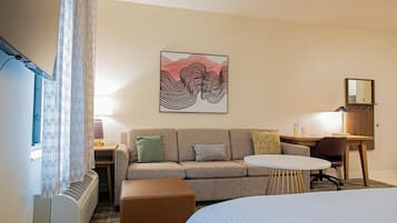 Et hotelværelse med sofa, rundt bord, skrivebord og seng.
