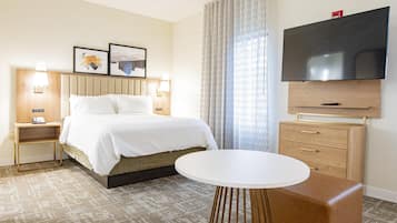 A hotel room with a bed, bedside tables, a TV, a small table, and a large window with curtains.