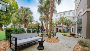 A courtyard with a bench, tables, palm trees, and a building with large windows. - Staybridge Suites Lafayette by IHG (Lafayette)
