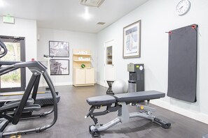 A gym with exercise equipment, a bench, a wall clock, and framed pictures. - Staybridge Suites Lafayette by IHG (Lafayette)