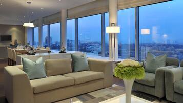 A modern living room with a sofa, a coffee table, and a view of a cityscape through large windows.