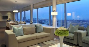 Una sala de estar moderna con un sofá, una mesa de centro y vistas a un paisaje urbano a través de amplios ventanales.