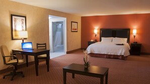 Ein Hotelzimmer mit einem Bett, einem Schreibtisch mit einem Laptop, einem Sessel, einem kleinen Tisch mit einer Vase und einem Nachttisch mit einer Lampe.