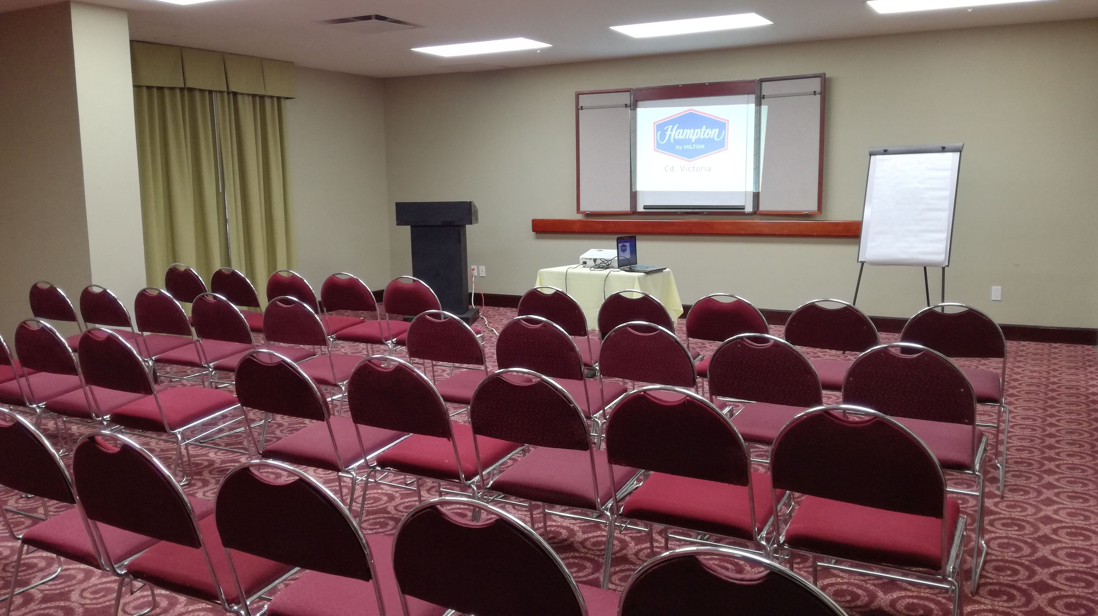 A conference room with rows of red chairs, a projector screen, and a podium.