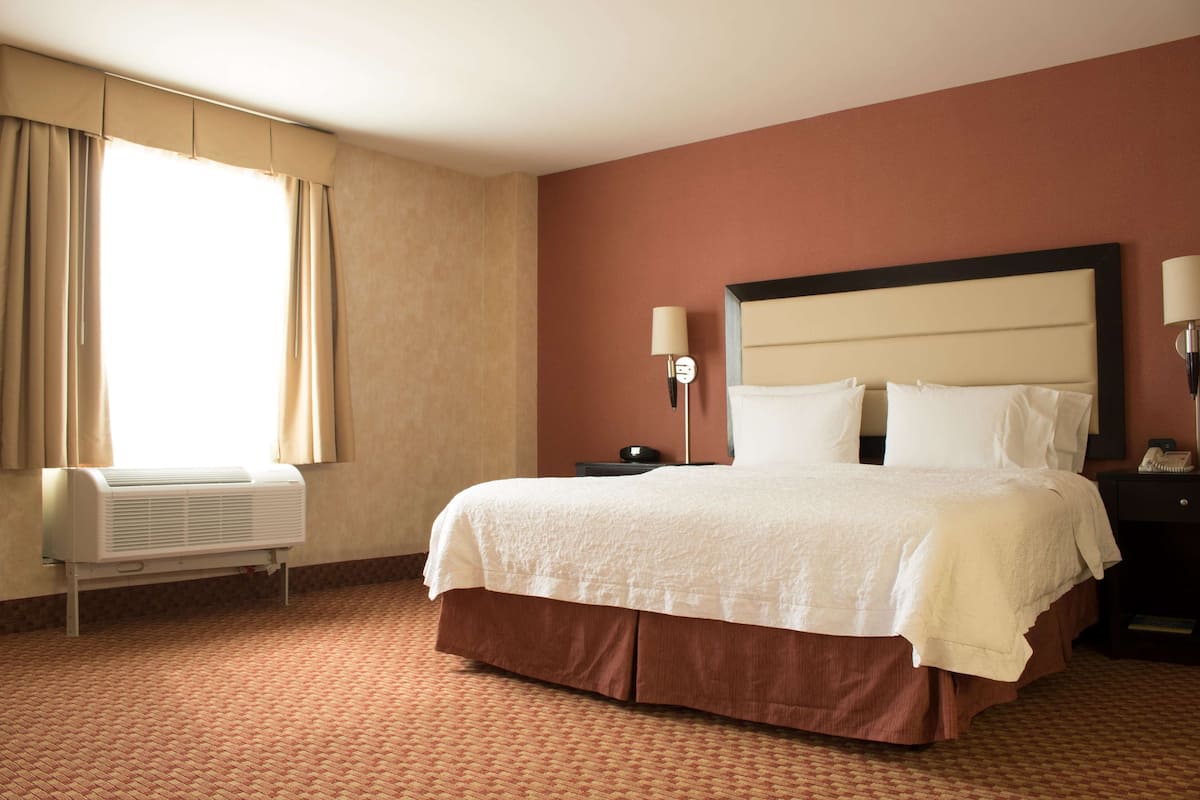 Una habitación de hotel con una cama grande, una mesita de noche, una lámpara y un equipo de aire acondicionado.