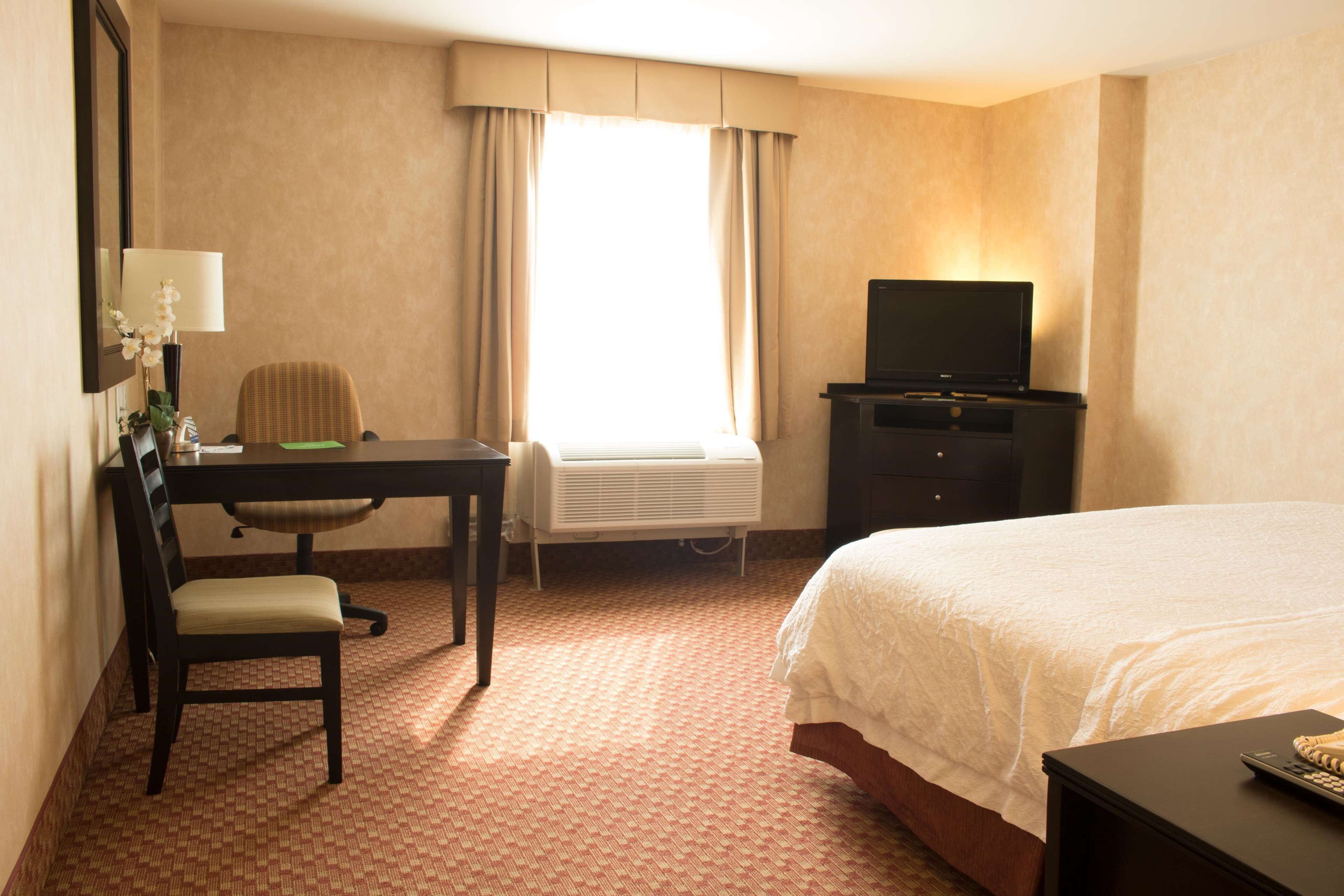 Una habitación de hotel con cama, escritorio, silla, televisor y aire acondicionado.
