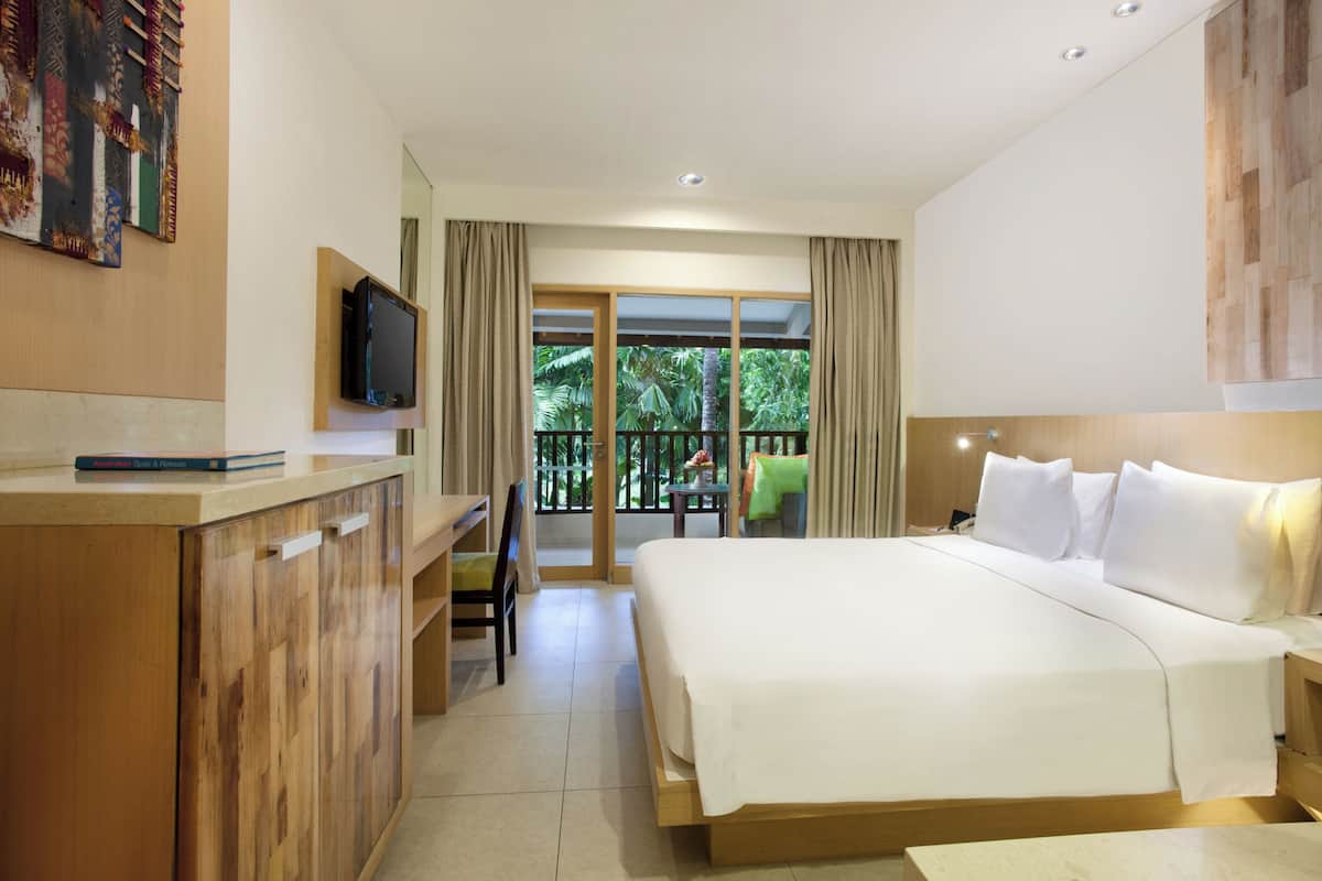 Une chambre d’hôtel avec un grand lit, un bureau avec une télévision et un balcon donnant sur un paysage verdoyant.