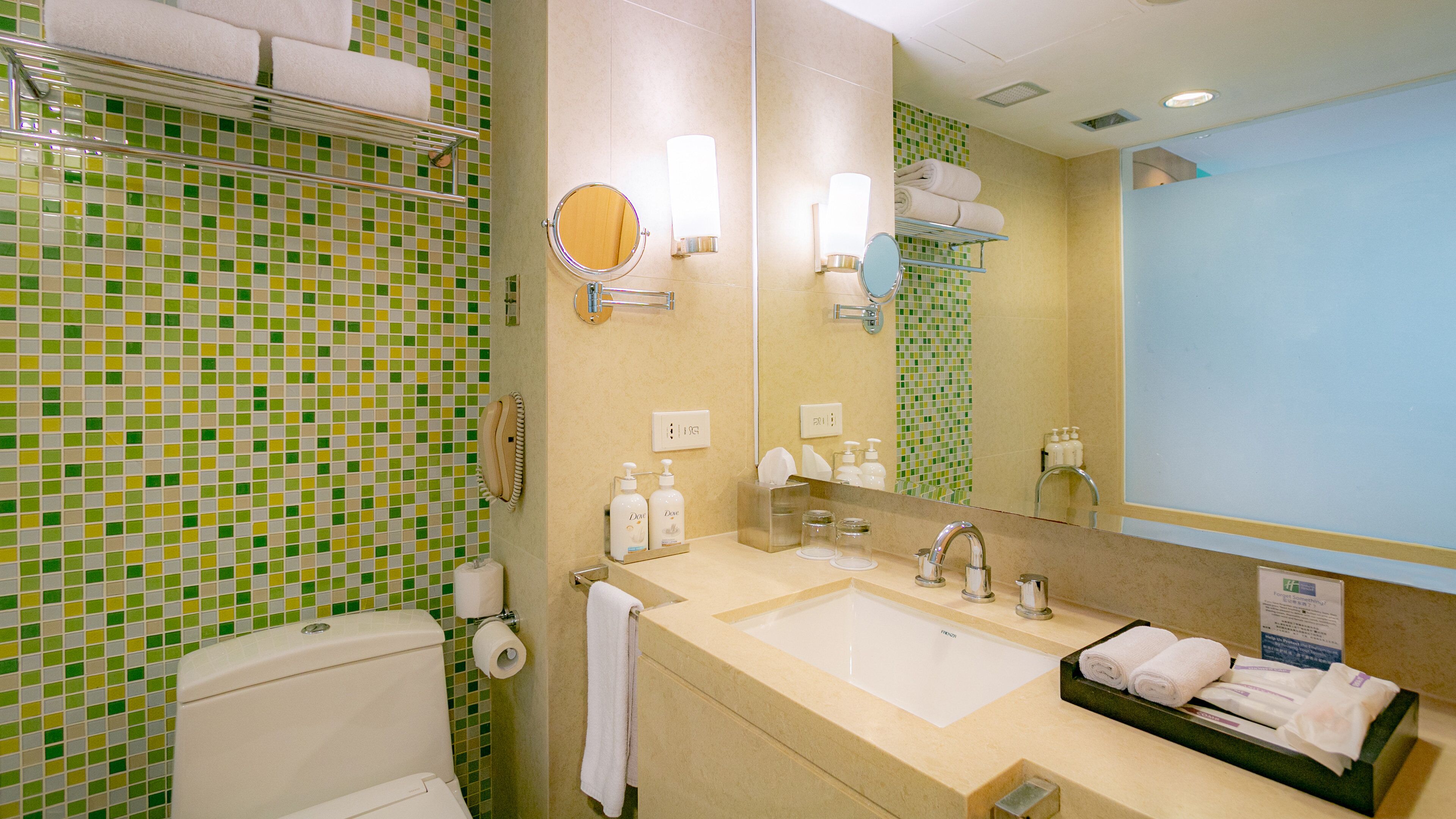 Bagno con WC, lavandino, specchio, portasciuga asciugamani e parete con mosaico verde.