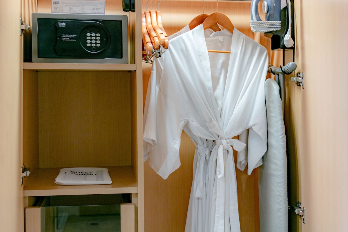 A robe hanging on a wooden hanger in a room with a microwave on a shelf and a hairdryer on a wall-mounted rack.