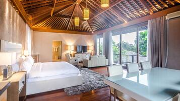 A hotel room with a large bed, a desk, a chair, a TV, and a balcony with a view of greenery.