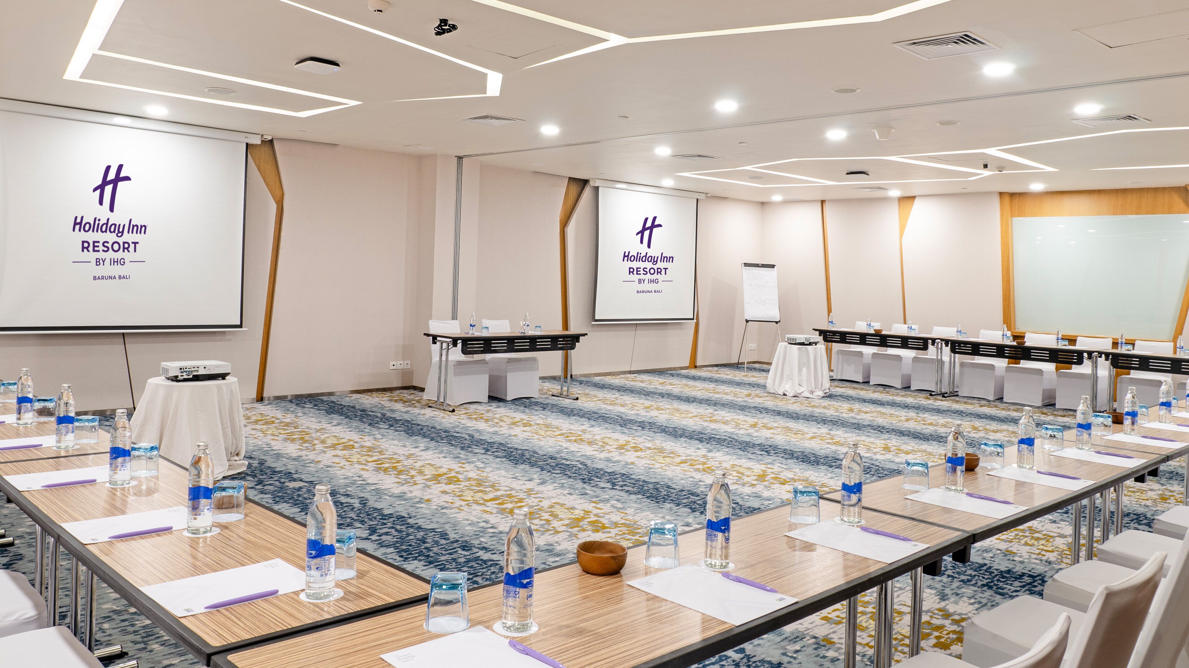 Een vergaderzaal in Holiday Inn Resort by IHG in Baruna Bali, met een vloerbedekking, tafels met waterflesjes en presentatieschermen.