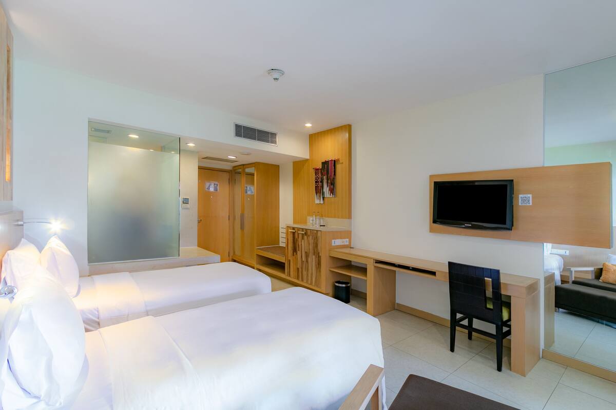 Une chambre d’hôtel avec deux lits, un bureau, une chaise, une télévision et un miroir.