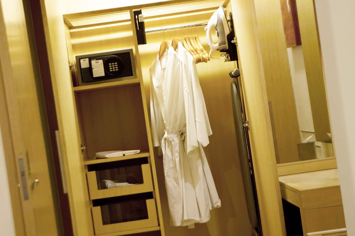 A wooden wardrobe with a mirror, a hairdryer, and a shelf with a white towel.