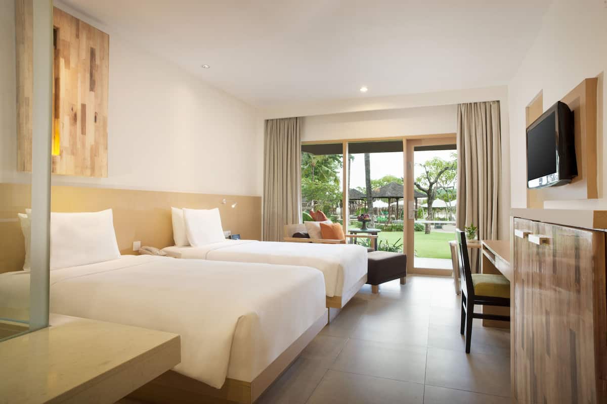 Une chambre d’hôtel avec deux lits, un bureau, une chaise, une télévision et une vue sur le jardin.