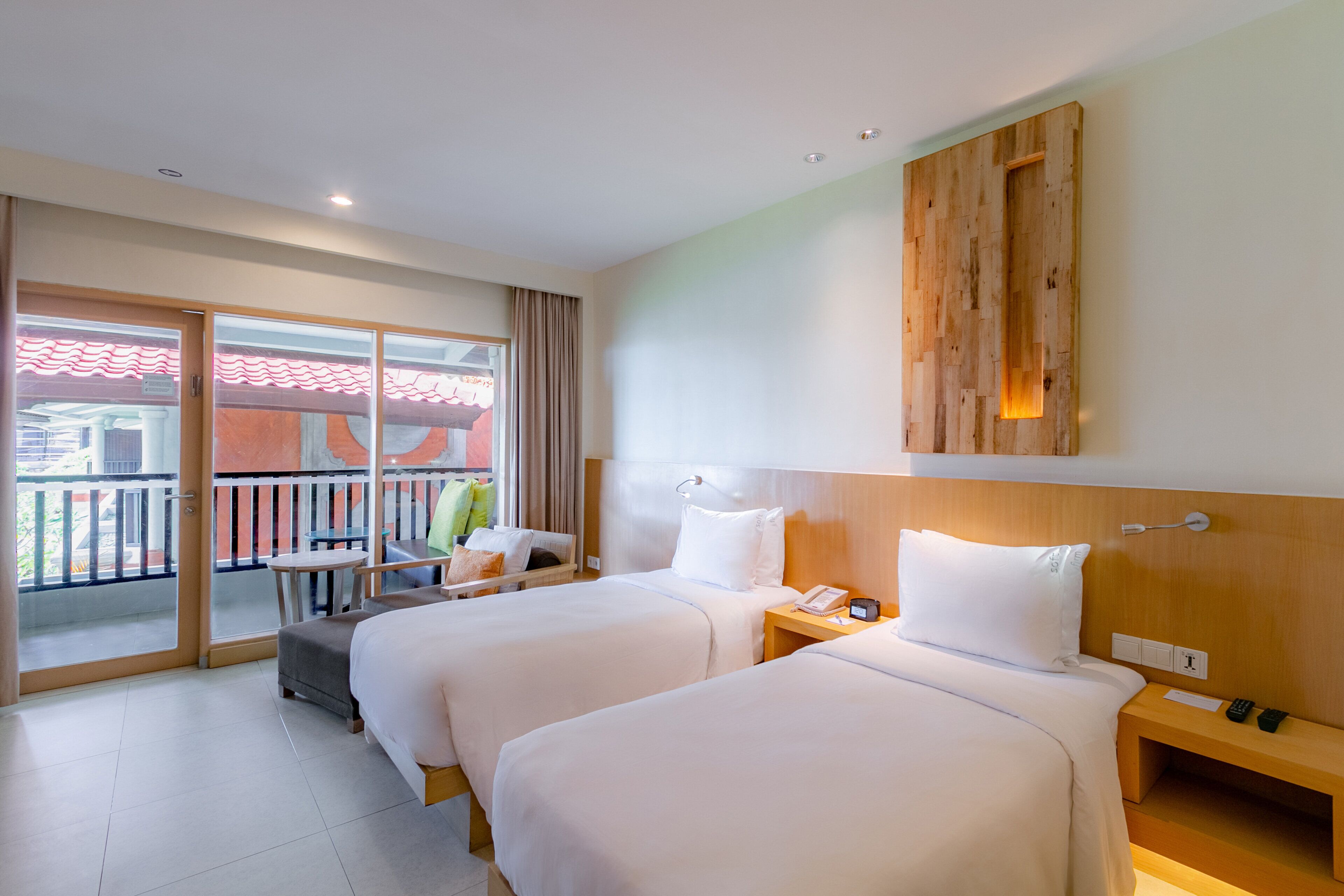 A hotel room with two beds, a wooden headboard, a small table, a chair, and a balcony with a view.