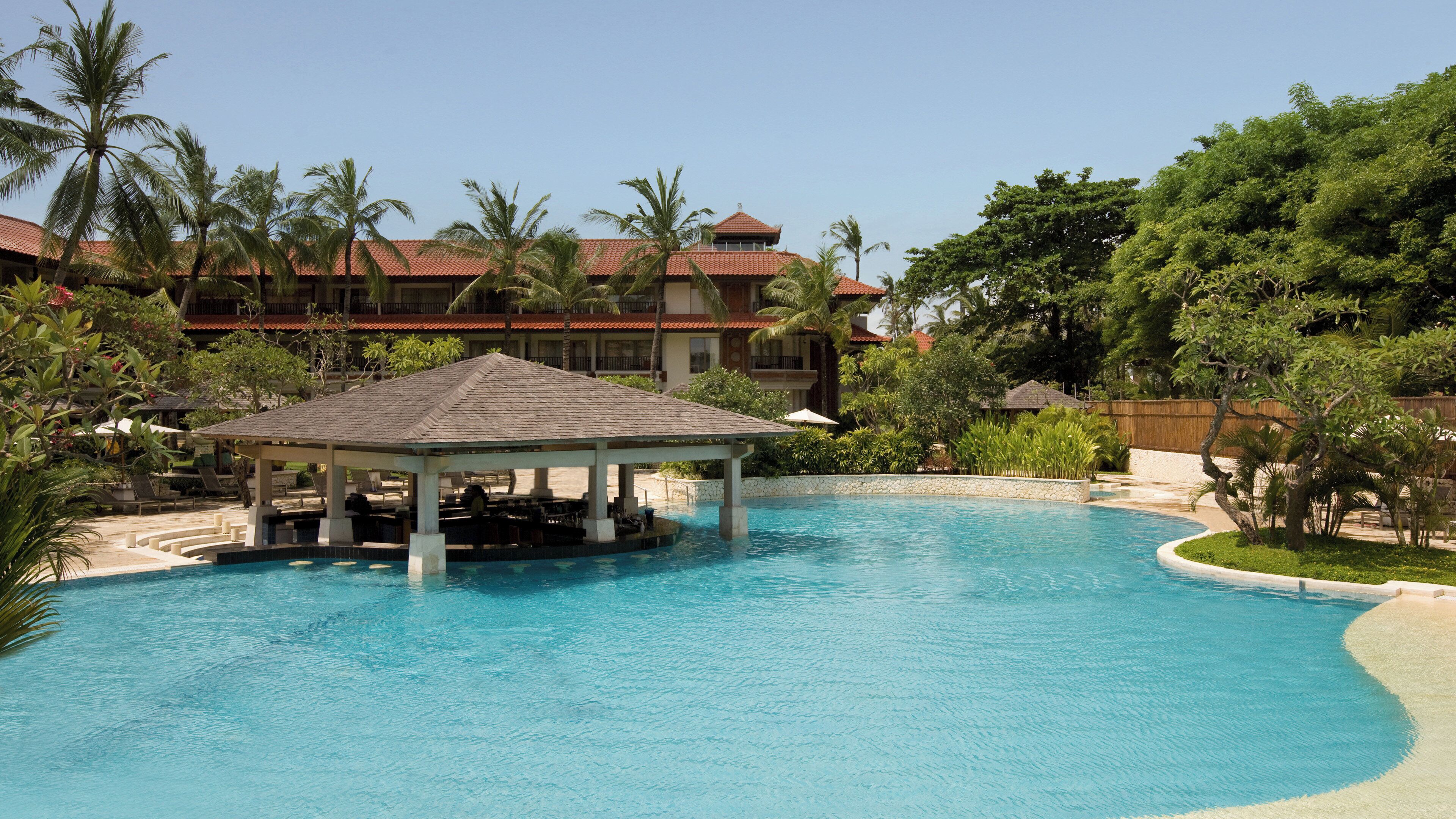 A resort pool with a gazebo, palm trees, and a building with a red roof.