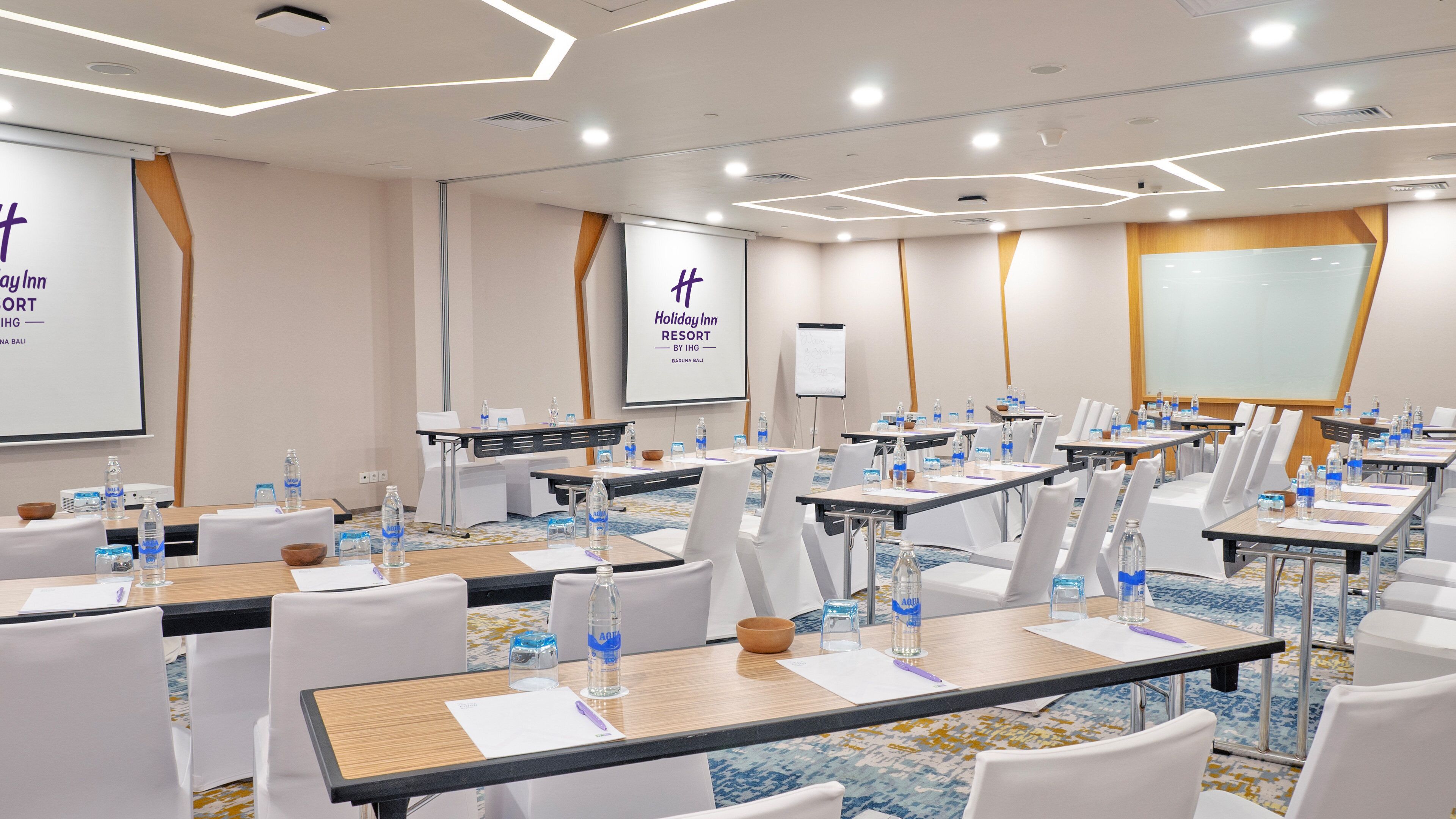 Una sala de conferencias con varias mesas, sillas y pantallas para presentaciones.