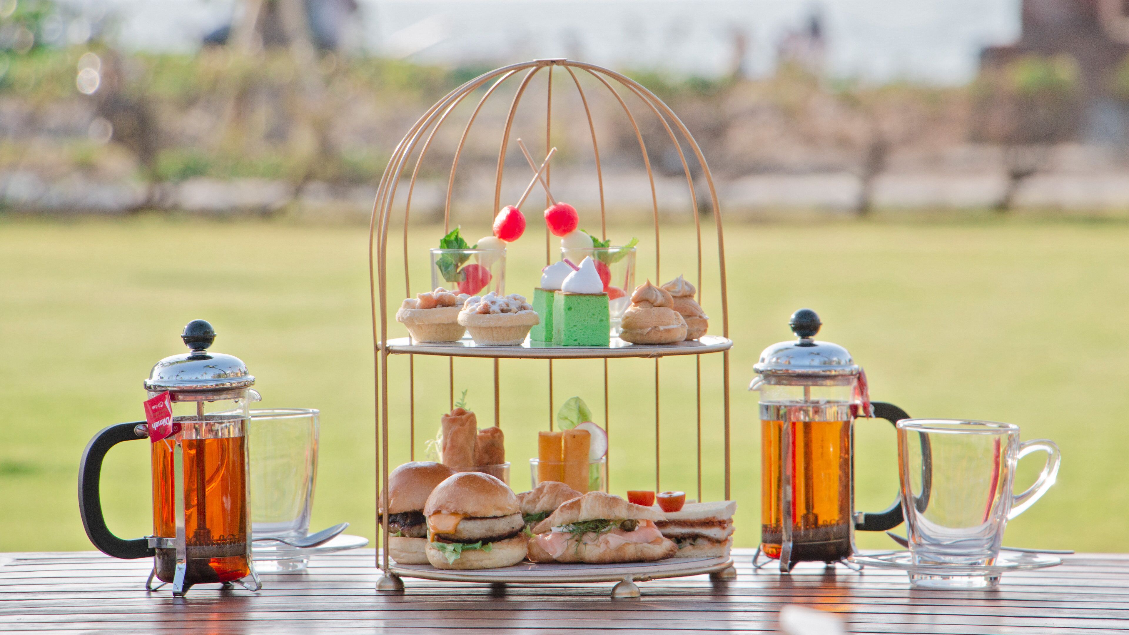 A picnic setup with a tiered stand holding sandwiches, a teapot, and a pitcher.