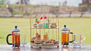 A picnic setup with a tiered stand holding sandwiches, a teapot, and a pitcher.