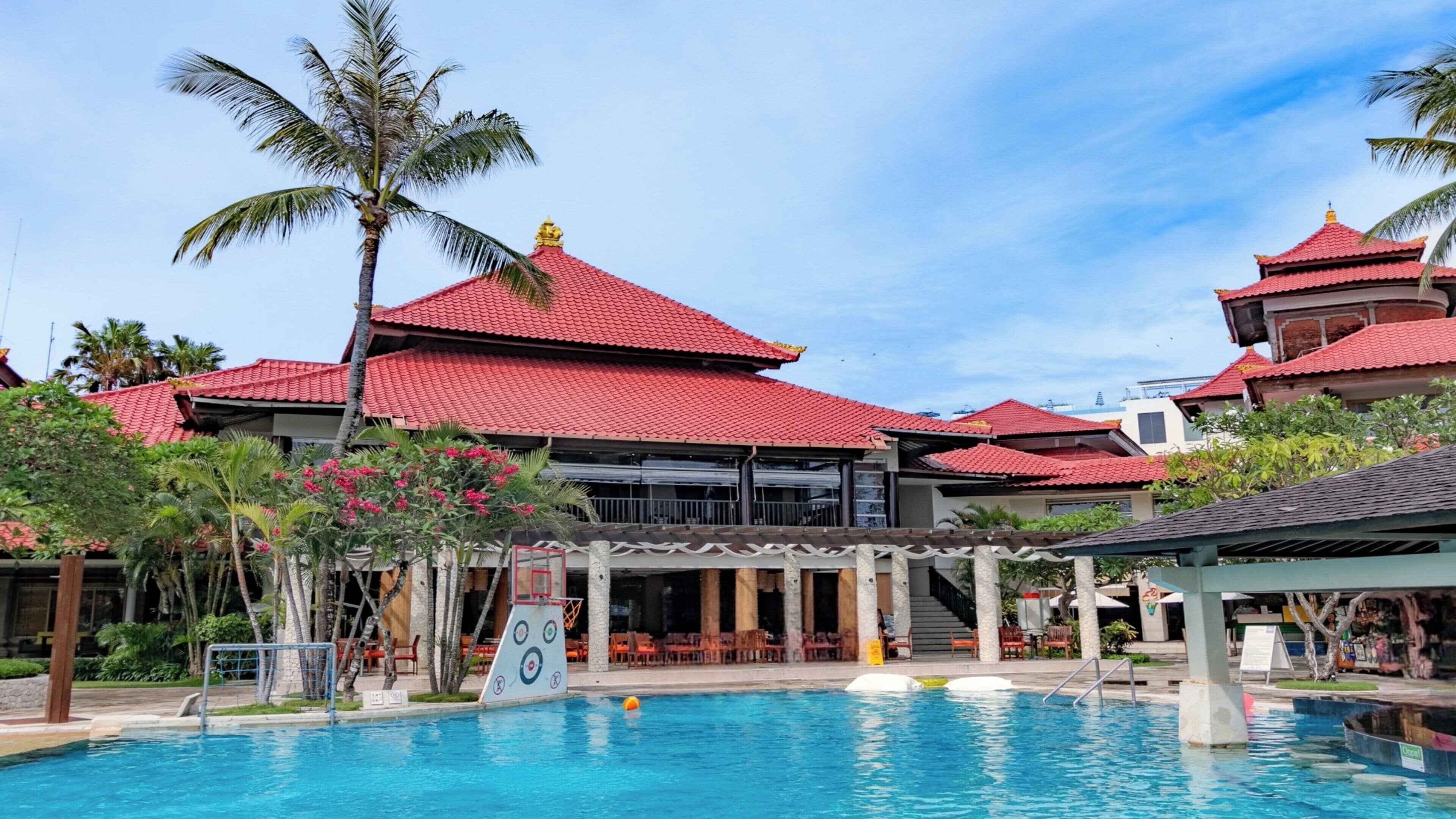 Um hotel com piscina, edifícios de telhado vermelho e palmeiras.
