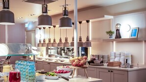 A modern kitchen with a buffet setup, including a fruit bowl, a juice dispenser, and neatly stacked plates and glasses. - Break Sokos Hotel Levi (Kittila)