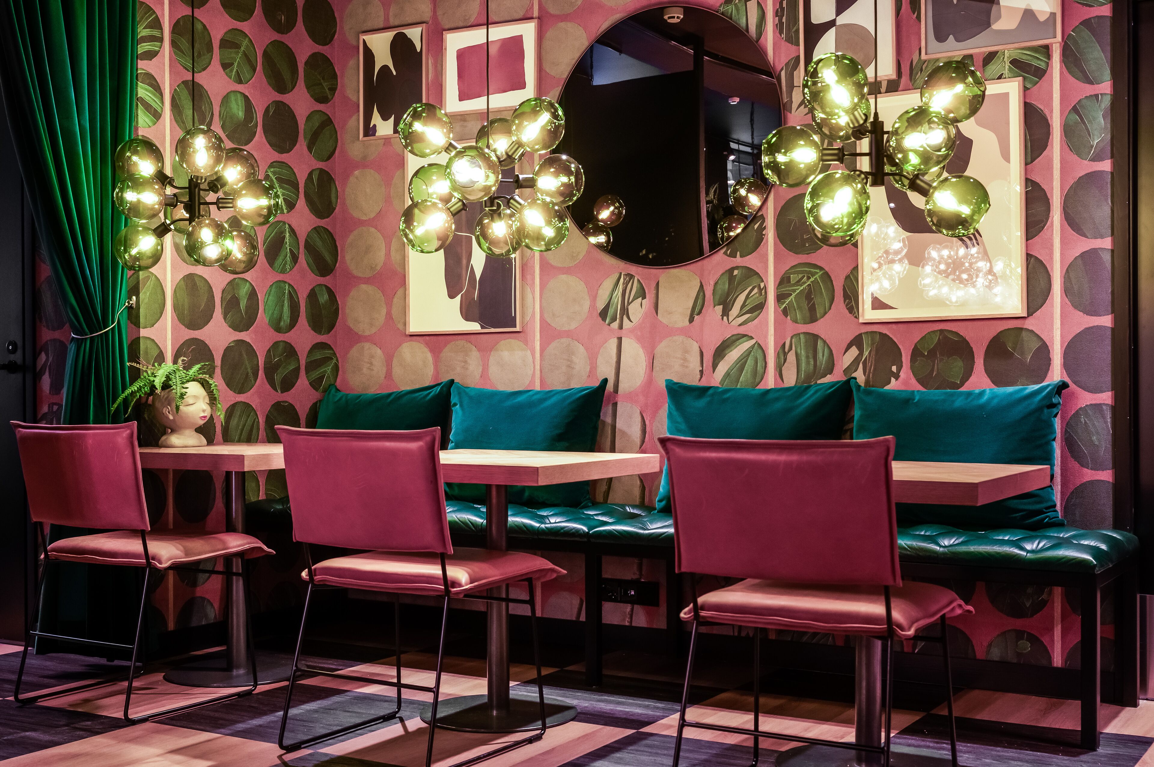 A restaurant interior with a checkered floor, green upholstered seating, and a wall adorned with circular patterns and a mirror.