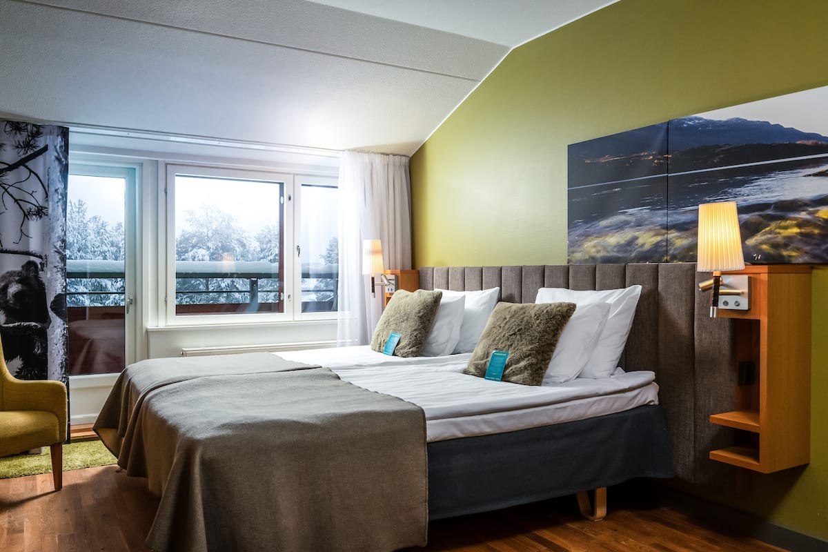 A bedroom with a bed, a nightstand, a lamp, and a view of a snowy landscape through a window.